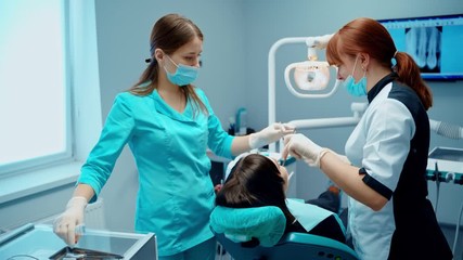 Patient at dentist's office. Female stomatologist together with assistant in medical uniform are treating woman's teeth in modern clinic.