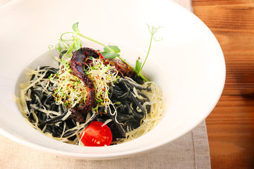 black pasta with octopus parmesan and cherry tomatoes on wooden background in white plate top view