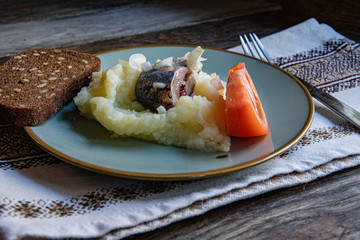 Cooking at home, in isolation, quarantine. Homemade rustic bread, herring, mashed potatoes, tomato in a plate on a wooden background in the home kitchen.
