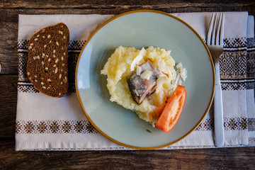 Cooking at home, in isolation, quarantine. Homemade rustic bread, herring, mashed potatoes, tomato in a plate on a wooden background in the home kitchen.