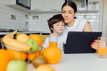 Family using a tablet pc in kitchen, mother with son happy smile, modern kitchen orange juice