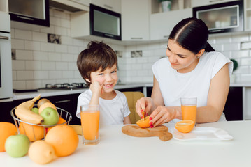 Beautiful happy mother pour orange juice to her child boy in kitchen