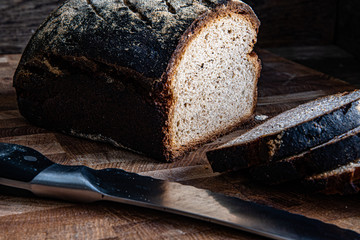 Homemade rustic sliced bread on a cutting kitchen board, knife on a wooden background.