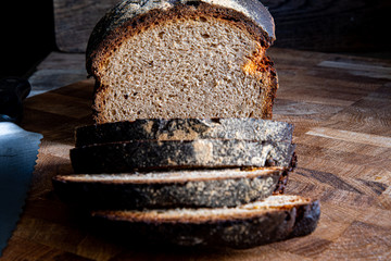 Homemade rustic sliced bread on a cutting kitchen board, knife on a wooden background.