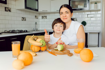 Mother and son sit in the kitchen and eat their hands. Fruit benefits concept. Healthy Eating.