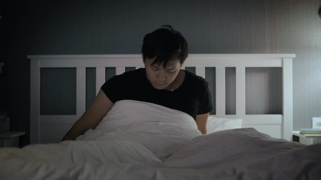Lazy young asian man waking up in the bed at home.