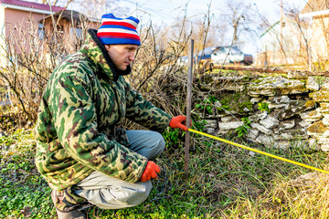 Man with measuring tape working on vegetable winter garden for post raised bed cold frame in Ukraine dacha