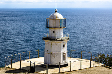 Fototapeta na wymiar Old lighthouse on a high cliff, sea horizon and sky, sunny day. Travel and adventure, tourism.