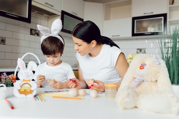 Mother and her son painting Easter eggs. Happy family preparing for Easter day.