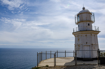 Fototapeta na wymiar Old lighthouse on a high cliff, sea horizon and sky, sunny day. Travel and adventure, tourism.