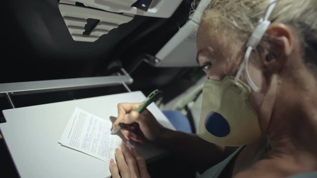 Woman travel caucasian at plane with wearing protective medical mask. Girl tourist at aircraft with protect respirator, fill out a registration form about her health. Coronavirus sars-cov-2 covid-19.
