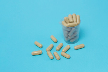 Some herbal capsules are in a plastic measuring cup on a blue background. Flat lay, top view.
