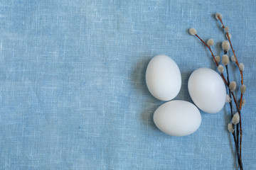 Three white chicken eggs and pussy-willow twigs on a blue tablecloth. Easter theme design.