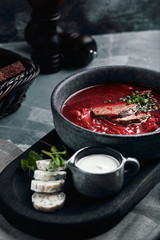 Ukrainian and Russian traditional beetroot soup - borscht in bowl with rib eye meat, rye bread, slices of bacon and sour cream on wooden background. Healthy food, top view, flat lay