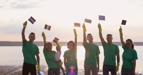 Volunteers in green T-shirts stand together and raise the flags of the European Union. Europeans are sorting recycled plastic. - Powered by Adobe