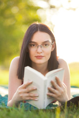 Fototapeta premium Beautiful girl lying in a park with a book. Outdoor leisure activity on a sunny summer day.