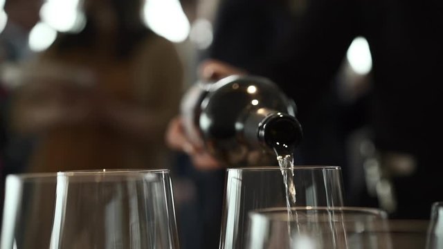 A waiter in a restaurant pours white wine from a bottle by the glass. Holiday, party or romantic dinner.