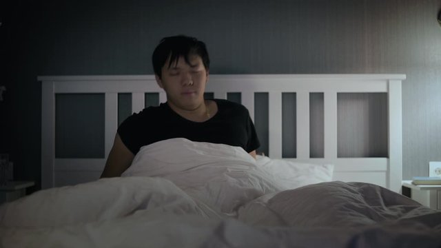 Sleepy young asian man waking up in the bed at home.