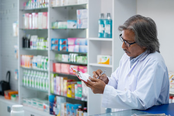 Professional senior Asian male Pharmacist checking medicines and health product inventory stock at hospital pharmacy or drugstore. Medical, pharmaceutics and personal healthcare concept.