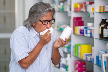 Asian senior man patient with dry cough and sore throat with symptom of cold or bronchitis disease looking for medicine to recovery illness in pharmacy. Medical, pharmaceutical and healthcare concept.
