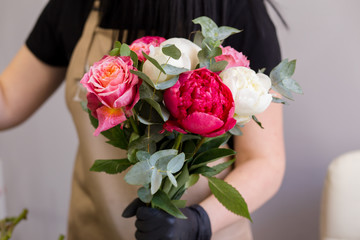 Obraz na płótnie Canvas florist in black gloves creates a bouquet of red peonies