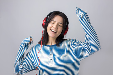 A young girl in a striped vest is listening to music in red headphones in a studio and dancing.