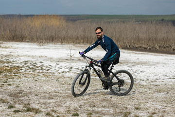 Cyclist in pants and fleece jacket on a modern carbon hardtail bike with an air suspension fork. .A guy with a bicycle on a salt lake.