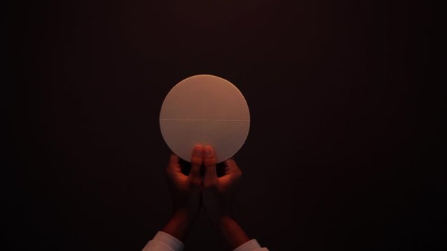 Hands of a priest raising holy communion bread