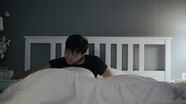 Young asian man waked up, looks on phone and jumped out of bed