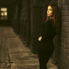 Sad young fashion woman in black dress leaning on brick wall