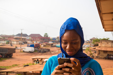 beautiful African muslim girl feeling excited as her is operating her cellphone.
