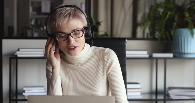 Confident female office worker wears headset conference video calling looking at laptop computer. Young businesswoman customer service manager speaking to webcam communicating in distance remote chat.