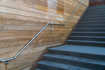 A metal stair handle attached to the wooden wall. Concrete stairs