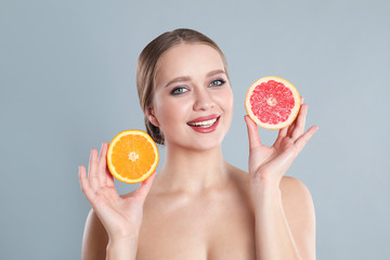 Young woman with cut orange and grapefruit on grey background. Vitamin rich food
