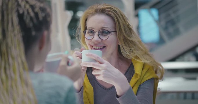 Mother and daughter talking relaxing at urban cafe. Two family generations enjoying hot coffee