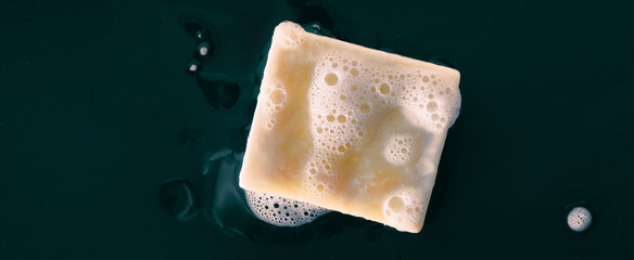 Bar of soap with foam bubbles on black background panoramic banner texture. Top view.