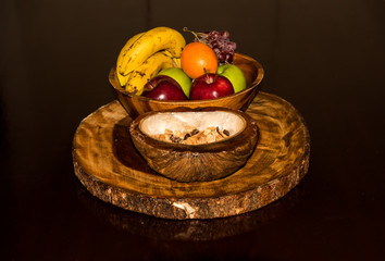 Fresh fruits and nuts presented in a coconut bowl on top of a wooden slab. 