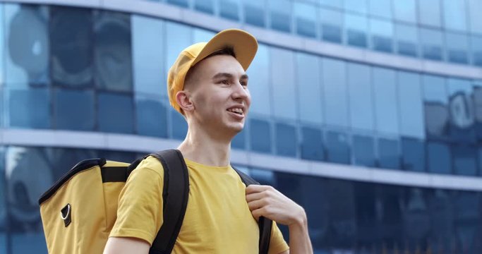 The delivery guy puts on a baseball cap and looks around on the background of the glass business center.