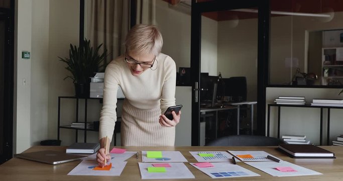 Young business woman designer holding smart phone communicating by video conference call planning work at distance corporate meeting. Remote worker talking with team in mobile videoconference chat.