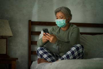 Fototapeta premium worried middle aged woman 50s with grey hair and protective mask checking online news with mobile phone during covid-19 virus home lockdown quarantine
