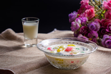 Colorful sweet rice gnocchi in fresh coconut milk in glass bowl on brown tablecloth on blackground. Delicious Thai desserts.