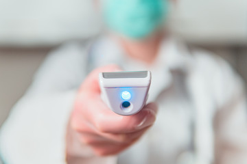 COVID-19 testing. Unrecognizable female doctor in protective suit, respirator mask holding laser digital thermometer. Checking the temperature