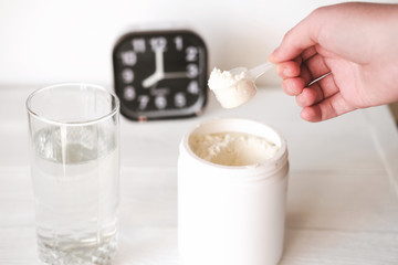 hand holding scoop of fish collagen. collagen peptides in container or jar. glass of water for mixing drink and alarm clock. Healthcare supplement concept. 