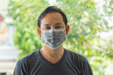 Portrait Asian man in gray t-shirt wearing a gray dust mask for protection virus and dust pollution with green nature blurred background.