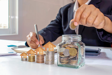 Close-ups of business women holding and putting coins in a bottle of money, including a house model on a pile of coins, ideas for saving money and real estate for investment.