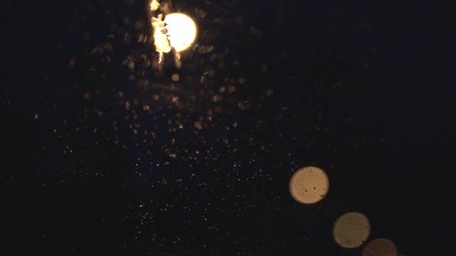 Raindrops dripping on a glass window with the bokeh of lights in the background - medium shot