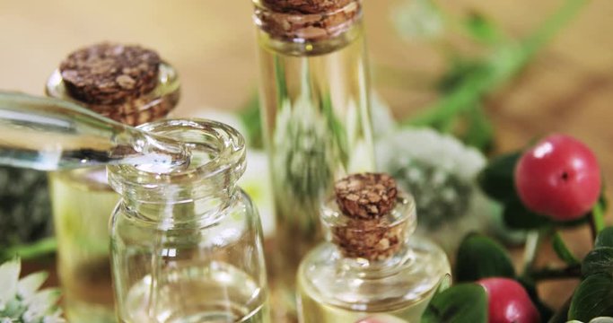 Perfumer making aroma liquids parfume pouring essential oil pipette to glass vial and closes cork cap, hand closeup. Fresh red and white flowers near bottles. Production of homemade perfume concept.