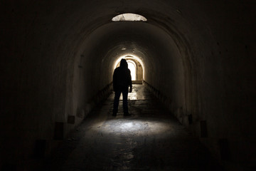 A man in dark clothes with a hood going to the exit of the light from a dark gloomy underground...