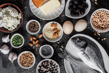 Set of source of calcium in products - fish, sesame, cheese, cottage cheese, poppy seeds, olives, flax seeds, eggs, legumes, almonds, garlic on a dark background, top view