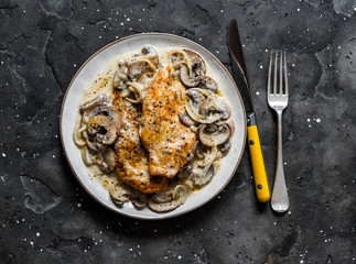 Fried chicken fillet with cheesy mushrooms cream sauce on a dark background, top view. Delicious homemade lunch